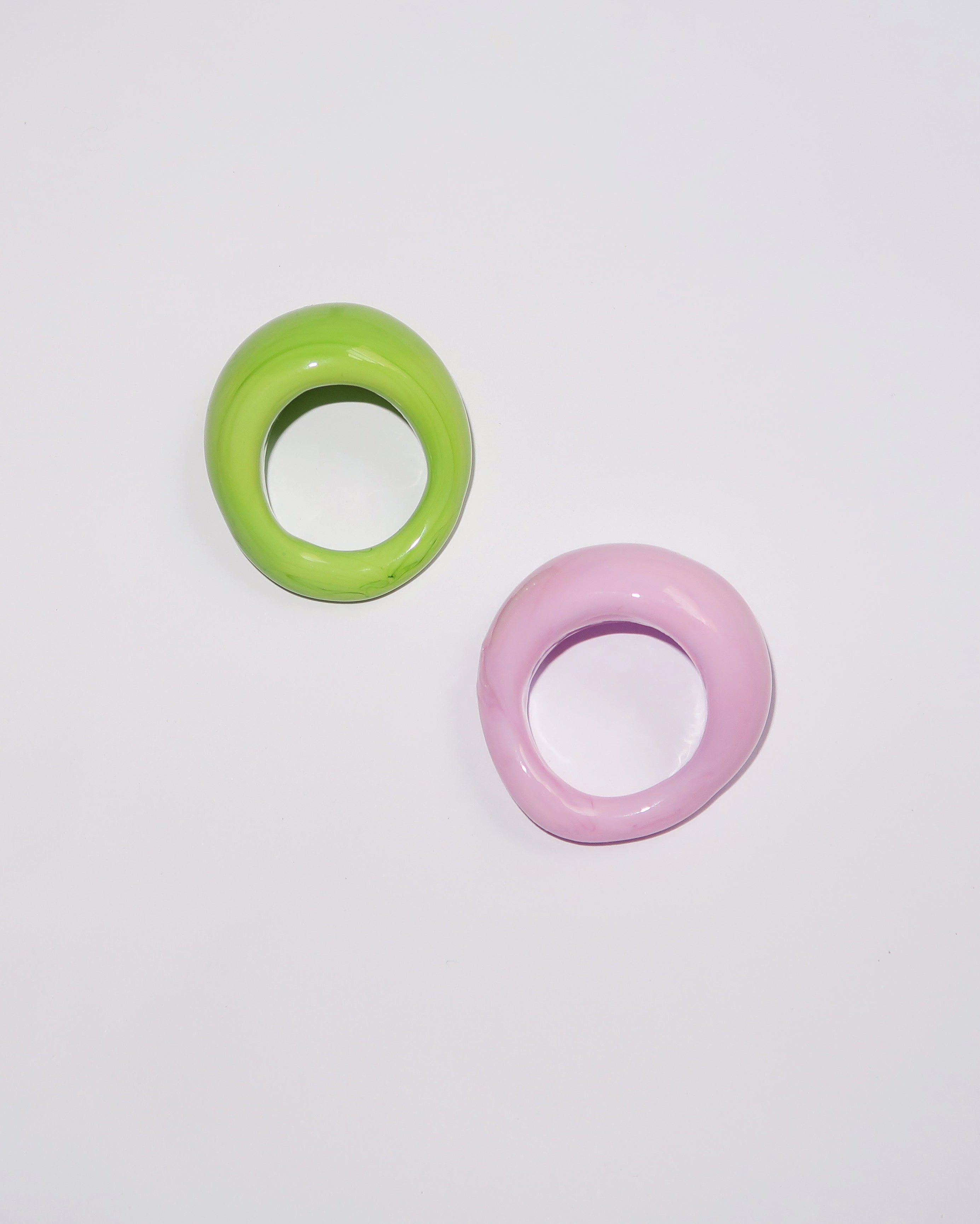Two glossy, thick ring-shaped earrings in lime green and pastel pink, displayed on a clean white background.