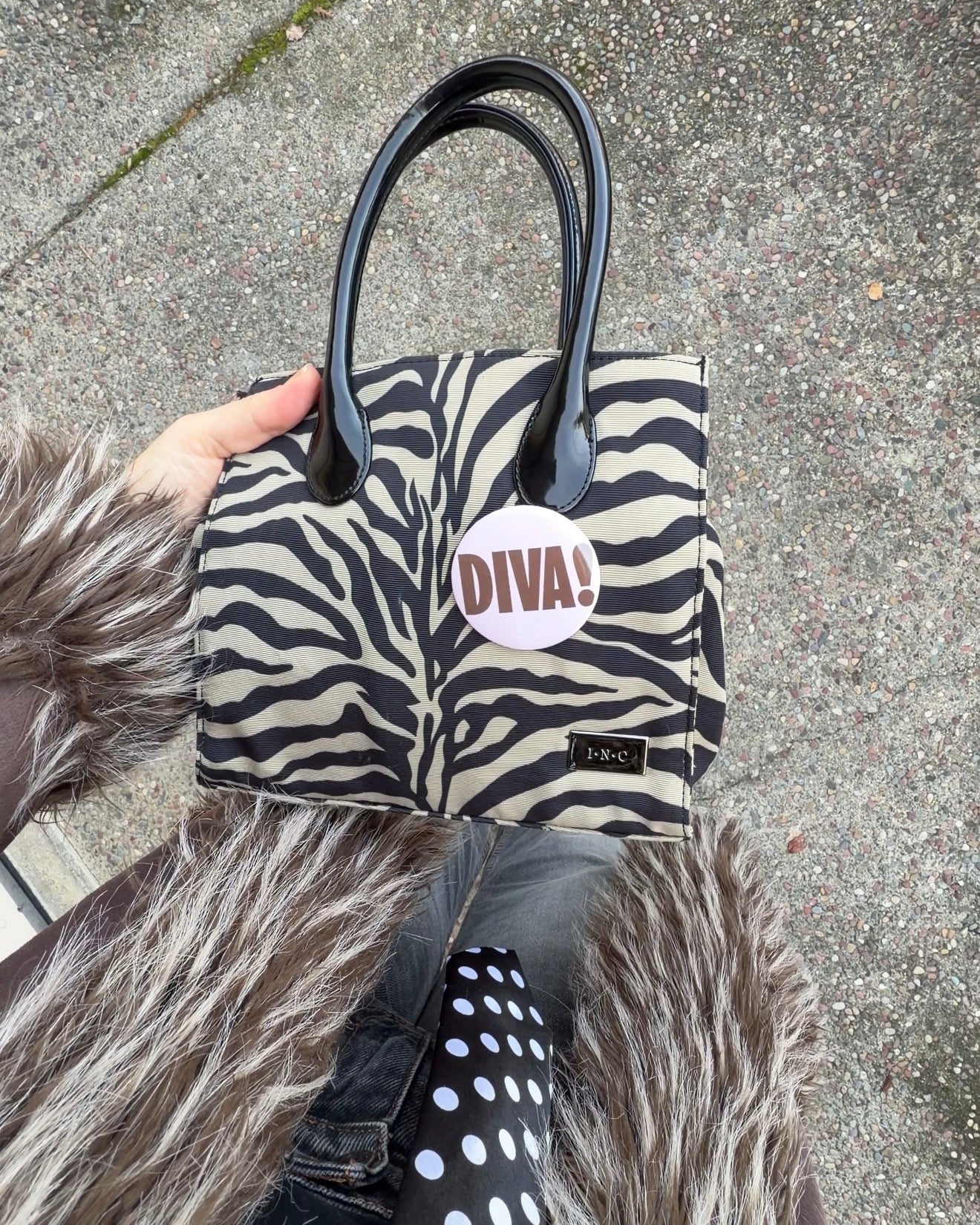 Zebra print handbag with 'DIVA!' label held by a person wearing a fur coat.