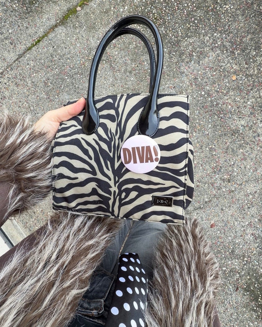 Zebra print handbag with 'DIVA!' label held by a person wearing a fur coat.