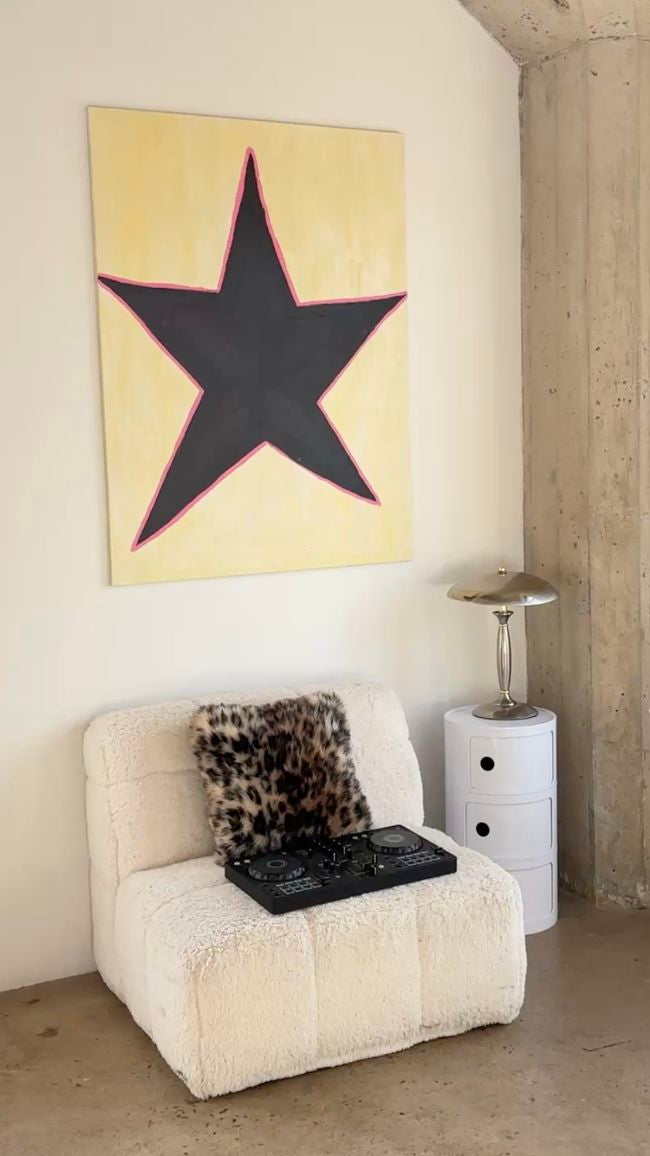 White armchair with a leopard print pillow and black tray, against a wall with a large star painting.